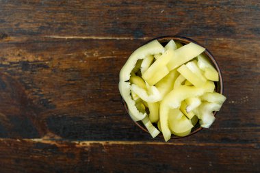 Ahşap arka planda bir kasede dilimlenmiş çiğ sarı biber. Sebze, malzeme ve zımba. Sağlıklı yemek..