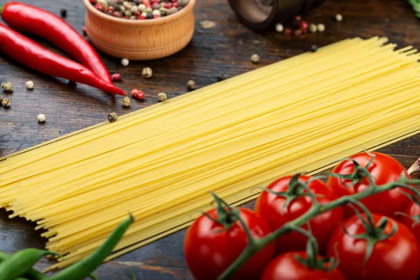 Taze domatesli çiğ makarna, biber, kuşkonmaz fasulyesi, baharat ve peynir ahşap bir masada. İtalyan spagettisi için yemek malzemeleri..