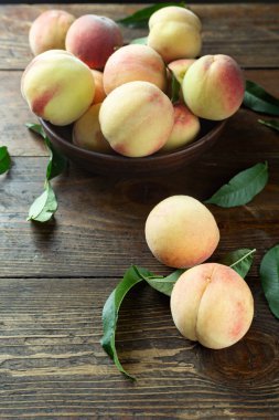 Ahşap bir kırsal masada, kil bir kasede taze şeftali hasadı. Şeftali yaprakları kompozisyonda mevcuttur. Organik meyve, vejetaryen yemeği..