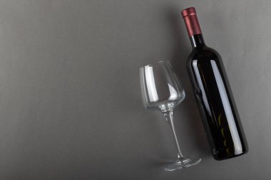 Mantarlı kırmızı şarap şişesi ve gri arka planda boş şarap kadehi. Alkolik içki. Şarap yapma konsepti. Mesaj için yer var. Üst görünüm.