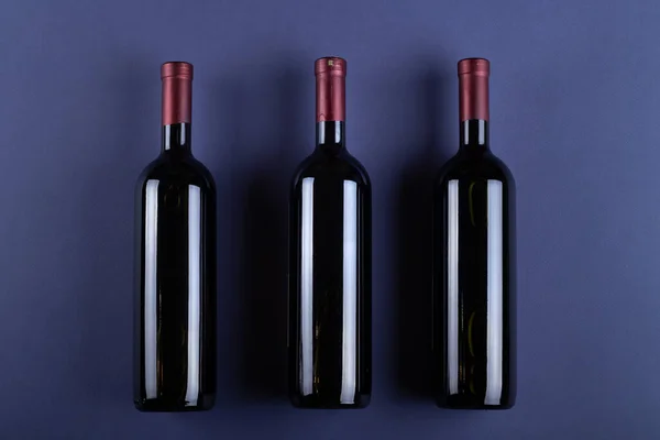 Three bottle of red wine without a label on a purple paper background. Mockup drink with place for you label and text. Space for text.