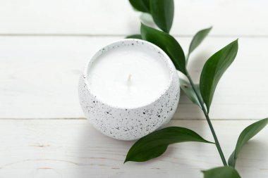 Bir mum ve beyaz bir masanın üzerinde bir bitki dalıyla kompozisyon. İç mekan. Metin için boşluk.