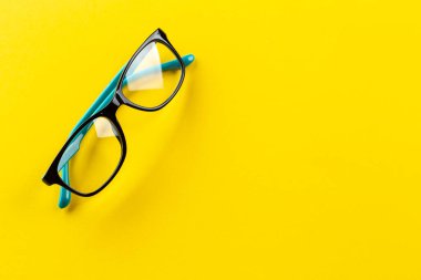 Stylish eyeglasses over yellow background. Glasses selection, eye test, vision examination at optician, fashion accessories concept. Top view, flat lay. Space for text. clipart