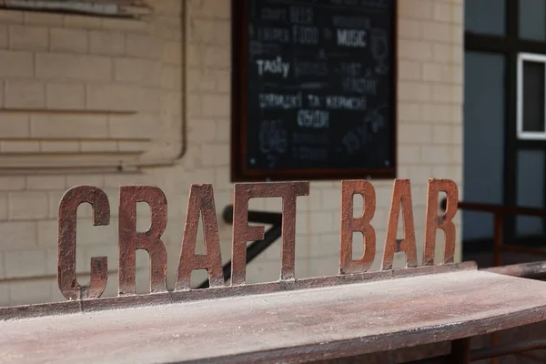 Iron signboard Craft Bar and bar counter. Entrance to a craft beer establishment. Blurred brick wall in the background.