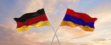 Almanya ve Ermenistan 'ın bayrakları rüzgarda dalgalanırken bayrak direkleri gökyüzüne karşı güneşli bir günde bulutlarla. İki ülke arasındaki ilişkiyi, diyaloğu sembolize ediyor. 3d illüstrasyon,