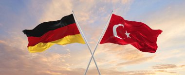 Almanya ve Türkiye 'nin bayrakları rüzgarda dalgalanırken bayrak direkleri gökyüzüne karşı güneşli bir günde bulutlarla. İki ülke arasındaki ilişkiyi, diyaloğu sembolize ediyor. 3d illüstrasyon,