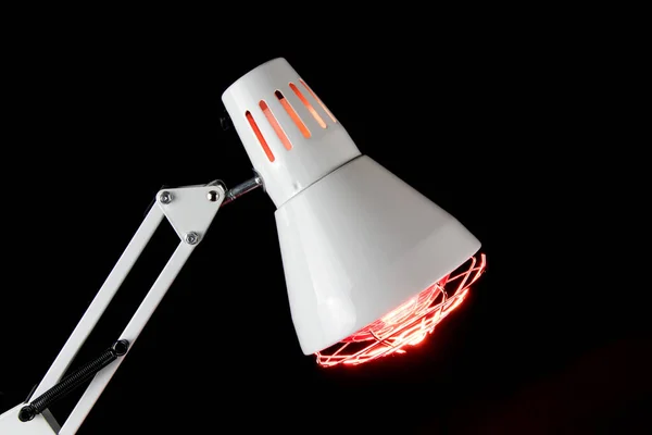 Closeup of illuminated infra red health lamp head isolated on a black background