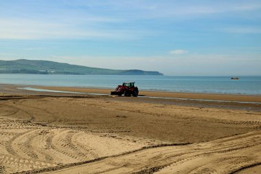 Traktör kumsalda çalışıyor, kumları düzleştiriyor.