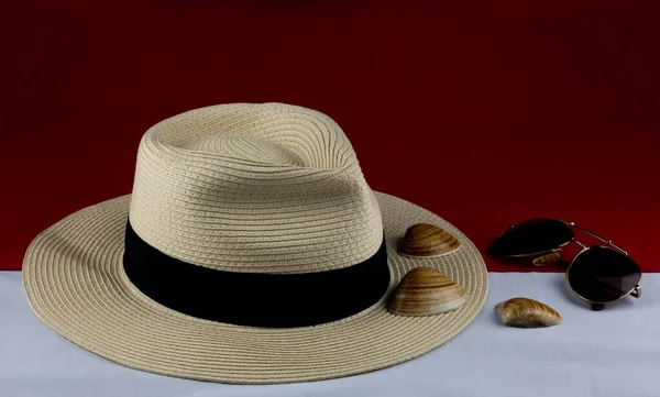 Sunglasses with panama hat and sea shells on a red and white base