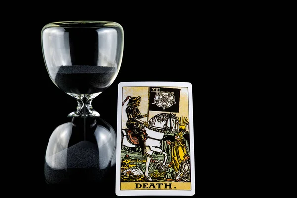 Death tarot card and hourglass isolated against a black background