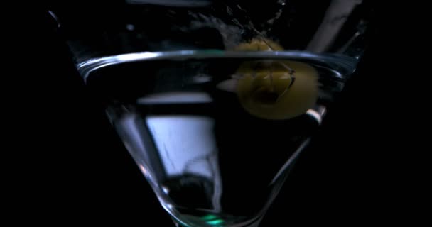 Oliv faller i ett glas med martini på en svart bakgrund — Stockvideo