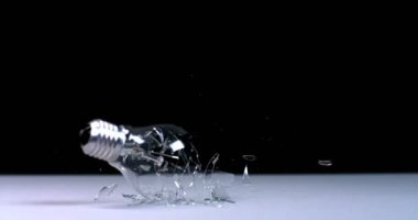 Bir ampul düşer ve siyah bir zemin üzerinde kırılır, uçan enkaz