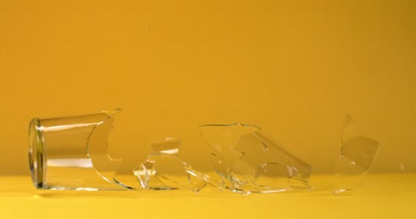 Vaso de vidrio cae y se rompe en pedazos sobre un fondo brillante sólido — Vídeo de stock