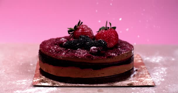 Azúcar en polvo que cae lentamente cubre un pastel de chocolate decorado con bayas — Vídeos de Stock