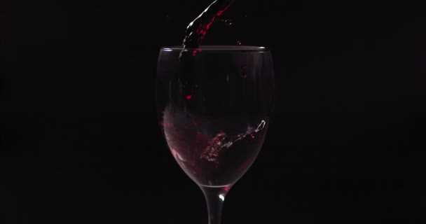 Primer plano del vino tinto vertiendo en la copa de vino en el fondo negro — Vídeos de Stock