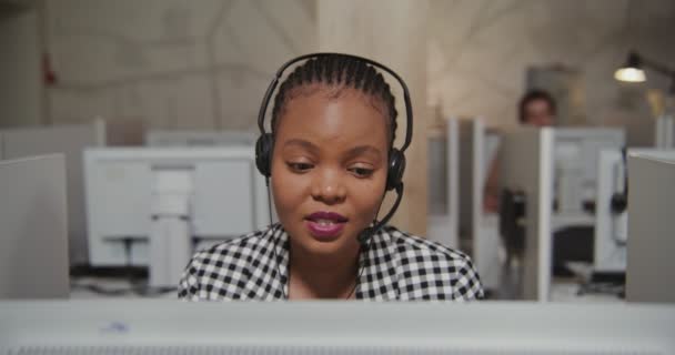 Працівник колл-центру афроамериканка в навушниках спілкується з клієнтом — стокове відео