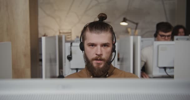 Trabajador del centro de llamadas: un joven con auriculares se comunica con un cliente — Vídeo de stock