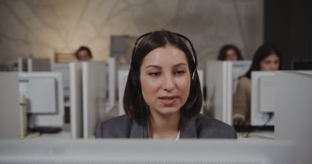 Працівник колл-центру молода жінка в навушниках спілкується з клієнтом — стокове відео
