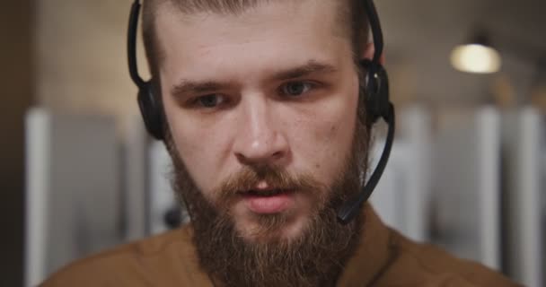 Trabajador del centro de llamadas: un joven con auriculares se comunica con un cliente — Vídeo de stock