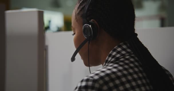 Сотрудница колл-центра африканская американка в наушниках общается с клиентом — стоковое видео