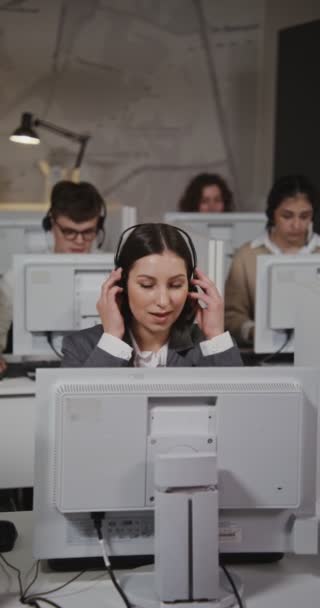 Trabalhador de call center - mulher jovem coloca fones de ouvido e começa uma conversa — Vídeo de Stock
