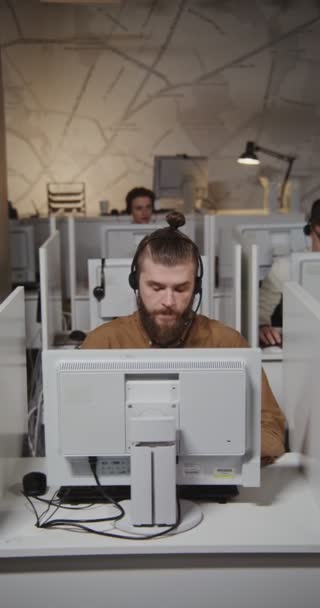 Trabajador del centro de llamadas: un joven con auriculares se comunica con un cliente — Vídeos de Stock