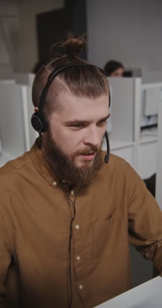 Call center worker - a young man in headphones communicates with a client — Stock Video