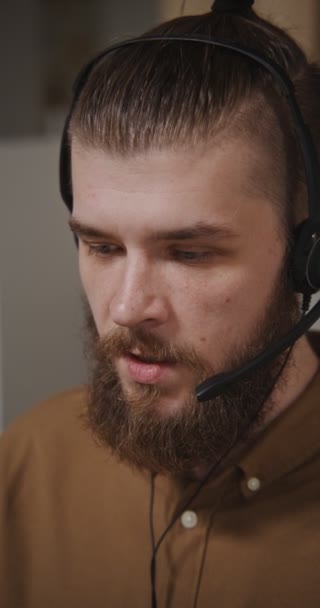 Çağrı merkezi çalışanı - kulaklıklı genç bir adam bir müşterisiyle iletişim kuruyor — Stok video