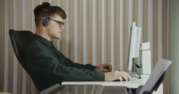Contact center munkavállaló - egy fiatal férfi a fejhallgató kommunikál egy ügyféllel — Stock videók
