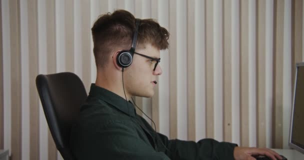 Trabalhador do centro de contato - um jovem em fones de ouvido se comunica com um cliente — Vídeo de Stock