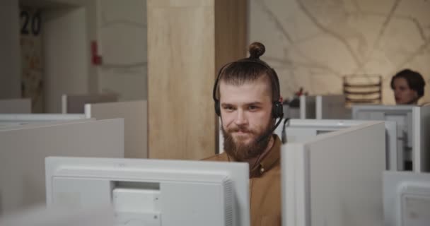 Call center lavoratore - un giovane uomo in cuffia comunica con un cliente — Video Stock