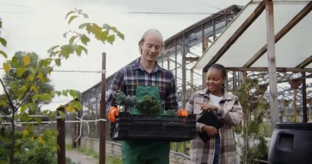 Erkek bir çiçekçi bir kutu çiçek taşıyor, yanında da Afro-Amerikalı bir kadın. — Stok video