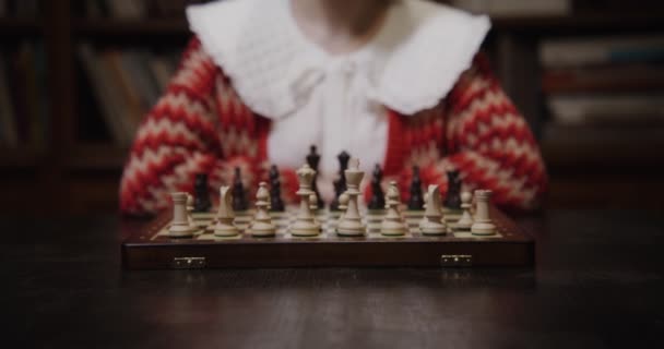 Een jonge vrouw speelt een schaakspel alleen, zittend aan een lange tafel in de bibliotheek — Stockvideo