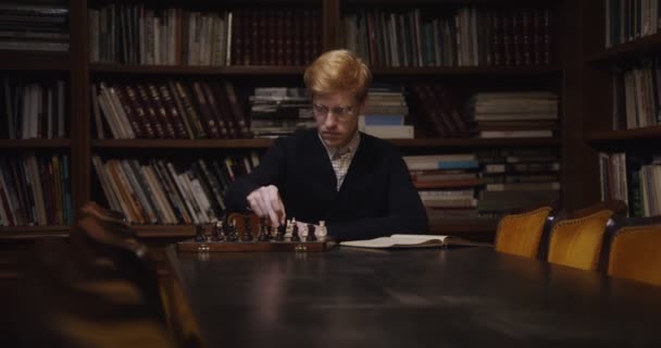 教科書を使って一人でチェスをする集中力のある男が勉強してる — ストック動画