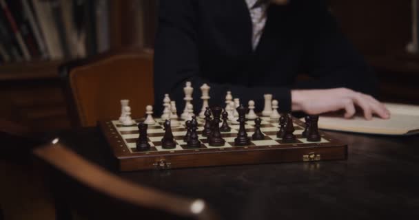 Ein Mann lernt konzentriert, um allein Schach zu spielen, mit einem Lehrbuch — Stockvideo