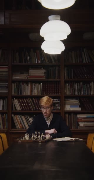 Ένας άντρας μελετάει με αυτοσυγκέντρωση για να παίξει σκάκι μόνος του, χρησιμοποιώντας ένα βιβλίο. — Αρχείο Βίντεο