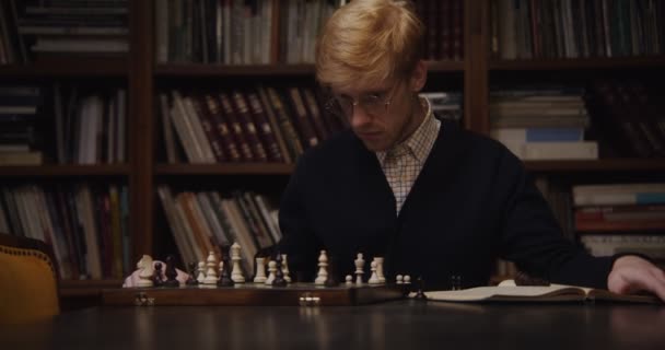 Чоловік вчиться з концентрацією, щоб грати в шахи самостійно, використовуючи підручник — стокове відео