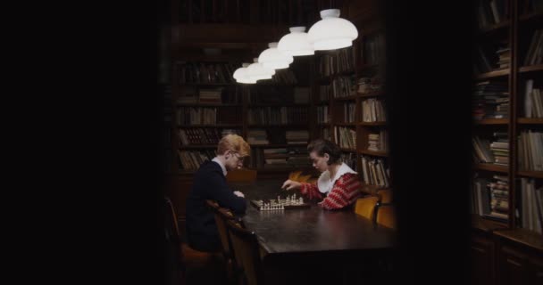 Egy férfi és egy nő elkezdenek sakkozni, egymással szemben ülve. — Stock videók