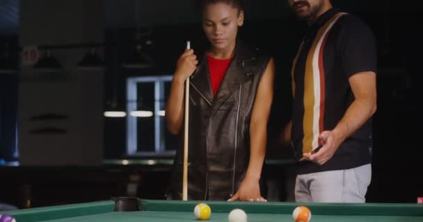 Een man legt uit en toont een jonge Afro-Amerikaanse vrouw hoe ze biljart moet spelen — Stockvideo