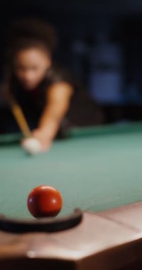Afro-Amerikalı bir kız bilardo oynarken topa işaret veriyor.