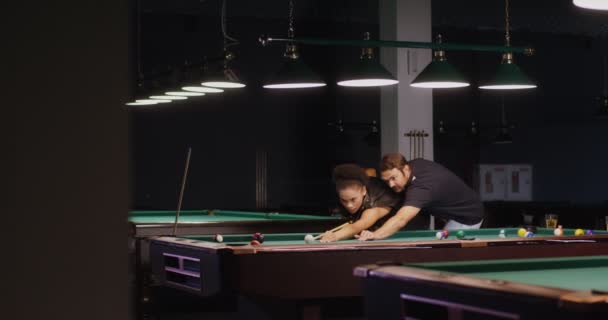 Un homme explique et montre à une jeune afro-américaine comment jouer au billard — Video