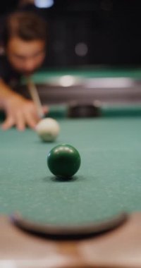 Bir adam dikkatle nişan alır ve bilardo topuna ıstakayla vurur, topu deliğe sokar.