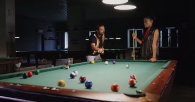 Genç bir adam ve kadın bilardo oynuyor, konuşuyor ve bira içiyorlar..