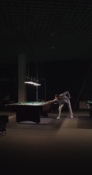 Um homem joga bilhar sozinho sob luzes escuras em um clube de bilhar — Vídeo de Stock