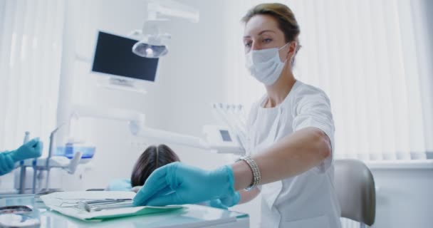Der Zahnarzt nimmt ein medizinisches Instrument und beginnt mit der Untersuchung der Patienten — Stockvideo
