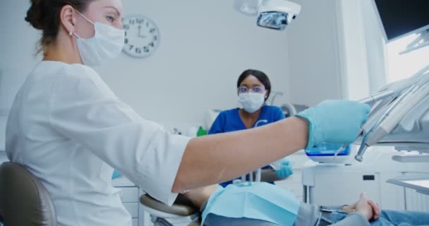 歯医者は歯の穴あけと治療を開始するための機械を取る — ストック動画