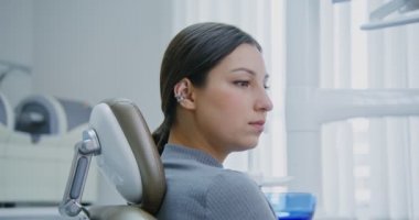 Dişçi koltuğunda oturan bir kadın doktor talimatlarını dinler.