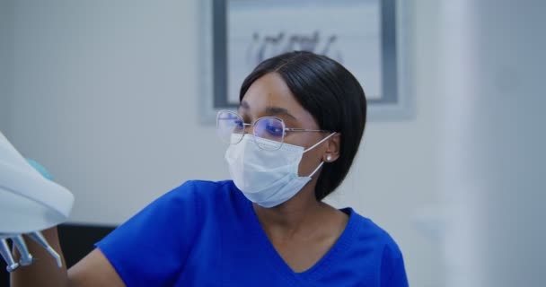 Dentista afroamericano toma taladro dental y comienza a perforar dientes de mujer — Vídeos de Stock