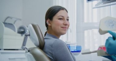 Dişçi koltuğunda oturan bir kadın doktor talimatlarını dinler.