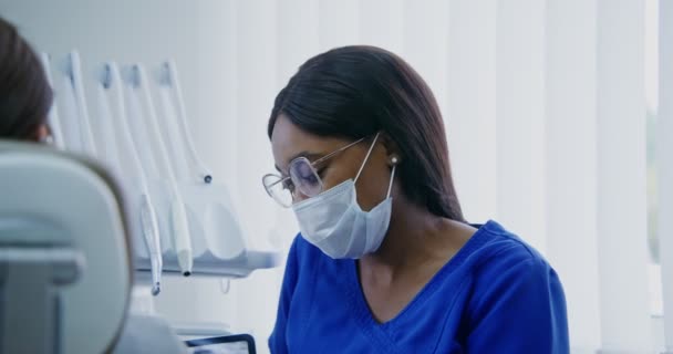 En tandläkare visar en kvinna en bild av tänder med hjälp av en tablett — Stockvideo